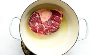 A thick beef shank, or osso buco in Spanish, is browning in a light-colored pot with oil.