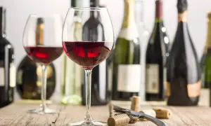 Two glasses of red wine, bottles, and corks on a wooden table. Imagine the rich, fruity mencia geschmack.