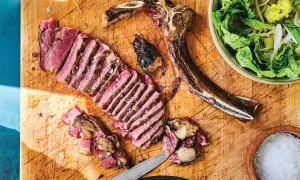 A perfectly cooked Spanish steak, sliced and ready to enjoy, sits on a wooden board with a side of fresh salad and a bowl of coarse salt.