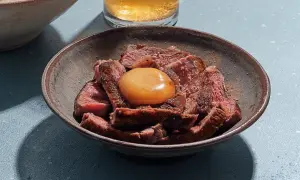 Sliced steak in a bowl topped with a glistening salt cured egg yolk, ready to be mixed into a rich, savory dish.