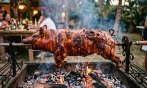 A whole spanish lechon, glistening and perfectly roasted, spins over glowing coals at an outdoor party.
