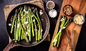 A pan of cooked asparagus with shaved parmesan and pine nuts, showing how to make asparagus a delicious side dish.