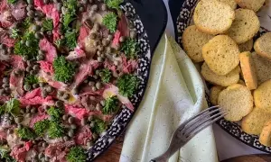 Thinly sliced beef carpaccio, adorned with capers and parsley, is served with toasted bread rounds.