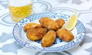 Crispy fried tiger mussels served on a blue and white plate with a lemon wedge and a glass of beer.