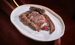 A perfectly cooked chuleton, a thick-cut bone-in steak, rests on a white platter, showcasing its juicy, red interior and seared crust.