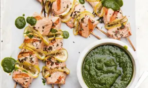 Grilled salmon skewers with lemon slices and a vibrant green sauce, ready to be dipped.
