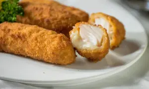 Golden cod croquettes, one split open to reveal flaky white fish and creamy filling, served on a white plate with a sprig of parsley.