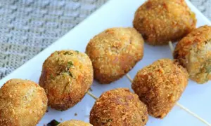 Golden-brown tuna balls on skewers, coated in crispy breadcrumbs, are arranged on a white platter.
