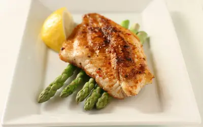 A perfectly seasoned fish fillet rests on a bed of asparagus, a lemon wedge on the side. A delightful dish inspired by Spanish fish recipes.
