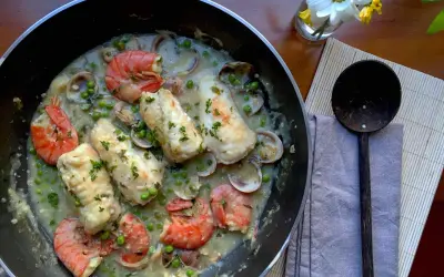 A delicious bonito fish recipe with prawns, clams, and peas in a creamy sauce, garnished with parsley.