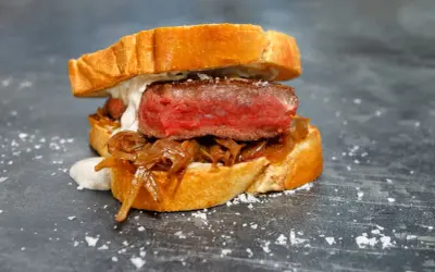 A juicy pepito de ternera, a tender steak sandwich on toasted bread with caramelized onions and a creamy sauce, sprinkled with sea salt.