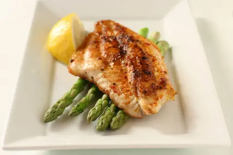 A perfectly seasoned fish fillet rests on a bed of asparagus, a lemon wedge on the side. A delightful dish inspired by Spanish fish recipes.