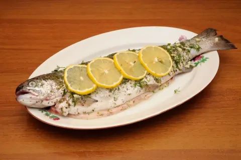 A whole trout, seasoned and garnished with lemon slices and herbs, ready to be cooked as trucha a la navarra.