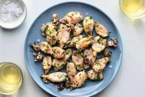 A plate of tender baby squid food, seasoned with herbs and served with a side of salt and white wine.