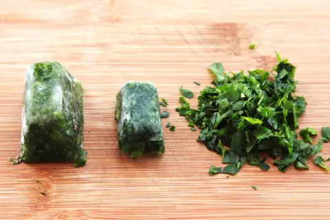 Learn how to freeze fresh herbs: two frozen herb blocks and a pile of chopped herbs on a wooden cutting board.