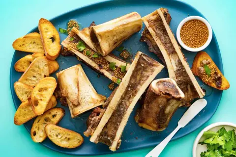Roasted bone marrow halves served with toasted baguette slices, whole grain mustard, and parsley. A delicious bone marrow recipe.
