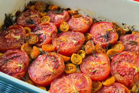 A baking dish filled with juicy, slow roasted tomatoes and cherry tomatoes, seasoned with herbs and spices.