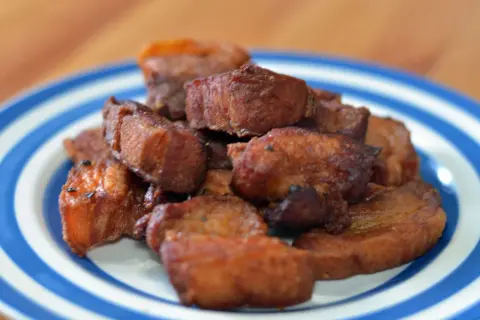 A pile of crispy fried pork belly, or chicharrones, on a blue and white striped plate.