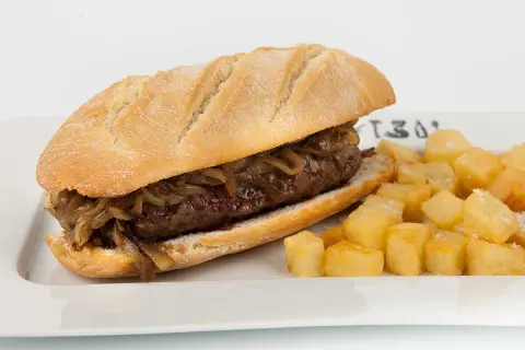 A pepito, a delicious steak sandwich with caramelized onions, served with crispy fried potatoes.