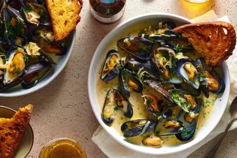 A delicious bowl of moules marinière, brimming with plump mussels in a creamy broth, served with crusty bread and a glass of beer.