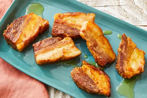 Crispy pork belly, Spanish style, glistening on a teal platter with a hint of green oil.