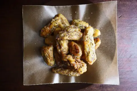 Crispy, golden fried morel mushrooms, lightly salted, piled on brown parchment paper. A delicious appetizer.