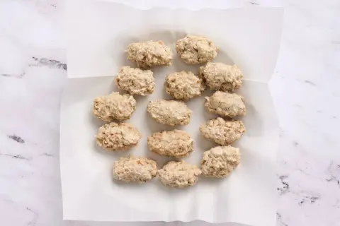 A dozen uncooked croquetas de pollo are arranged on white parchment paper, ready for frying.