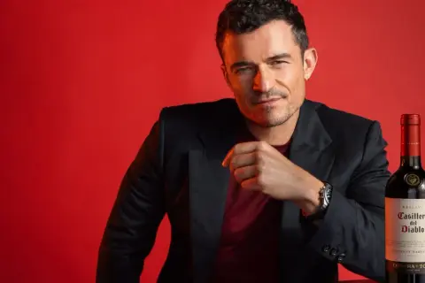 Orlando Bloom poses with a bottle of Casillero del Diablo Cabernet Sauvignon, hinting at its rich taste.