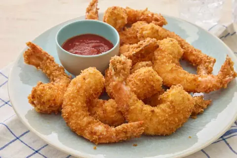 Crispy fried shrimp piled high on a plate, with a small bowl of red dipping sauce.