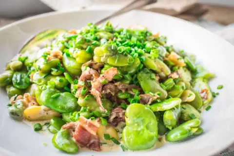 A delicious dish showing how to cook fava beans with bacon and chives, served in a creamy sauce on a white plate.