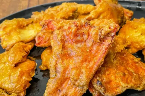 Crispy, golden-fried pieces, possibly part of a delicious chicken of the woods recipe, piled on a black plate.