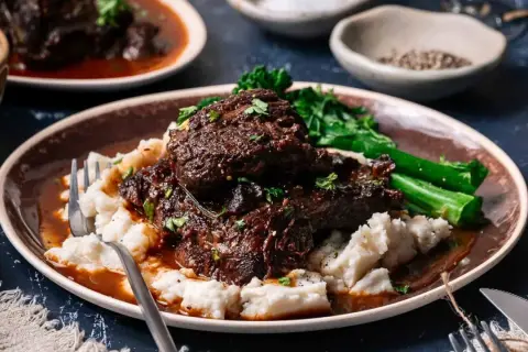 Tender beef cheek, Spanish style, served with creamy mashed potatoes and vibrant green vegetables.