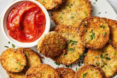 Crispy spanish fried eggplant slices, golden brown and seasoned, served with a side of vibrant tomato sauce and sprinkled with fresh parsley.