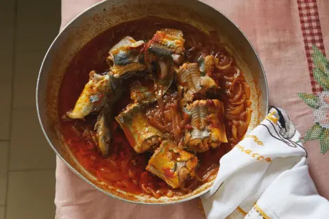 A rustic pan of eel recipes, featuring chunks of eel simmered in a rich, tomato-based sauce with onions.
