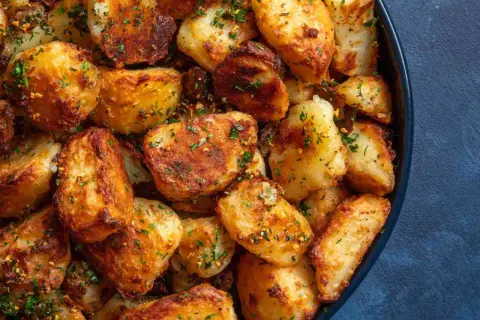Crispy, golden-brown roasted new potatoes, seasoned with herbs and spices, piled high in a dark blue bowl.