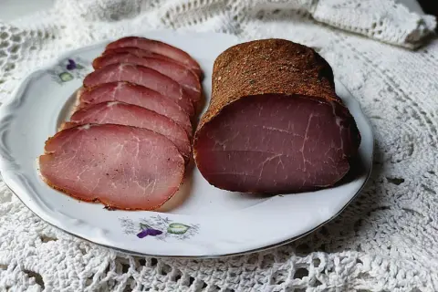 A whole and sliced cured pork loin, seasoned with spices, rests on a decorative plate.