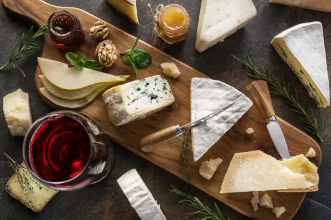 A beautiful spread of wine and cheese pairings, featuring a glass of red wine, various cheeses, pears, walnuts, and honey on a wooden board.