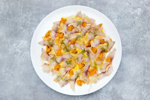 Thinly sliced sea bass crudo, glistening with olive oil and dotted with bright orange citrus segments and fresh dill.