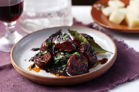 Delicious chorizo tapas, glazed and garnished with parsley, served with a glass of red wine and cheese.