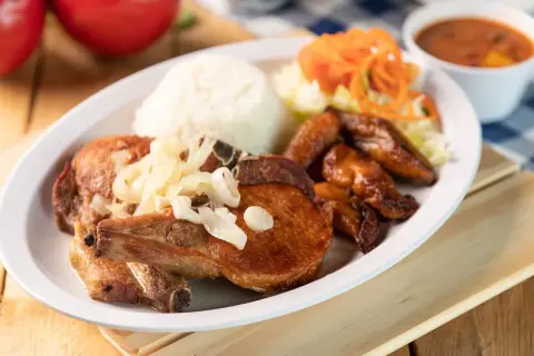 A delicious plate of chuleta meat, a flavorful pork chop, served with rice, fried plantains, salad, and beans.