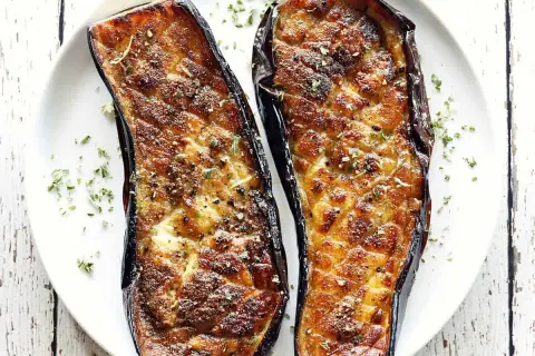 Two halves of baked eggplant, seasoned and sprinkled with herbs, are a delicious start to many eggplant recipes.
