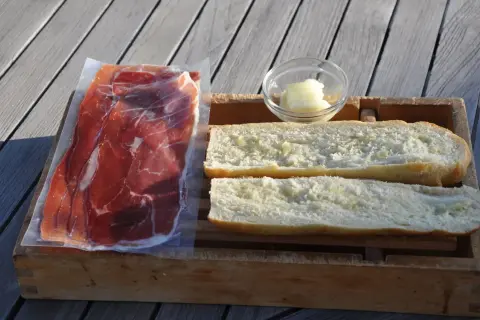 Ingredients for a delicious jamon iberico sandwich: thinly sliced cured ham, buttered bread rolls, and a small dish of butter.