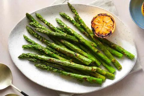 A plate of perfectly grilled spanish asparagus, lightly charred and served with a grilled lemon slice.