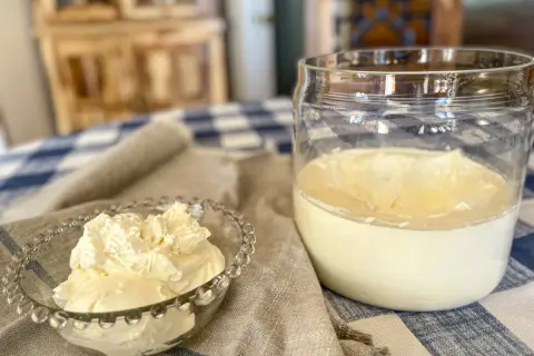 A small glass bowl overflows with fluffy crème fraîche, next to a jar of the creamy dairy product.