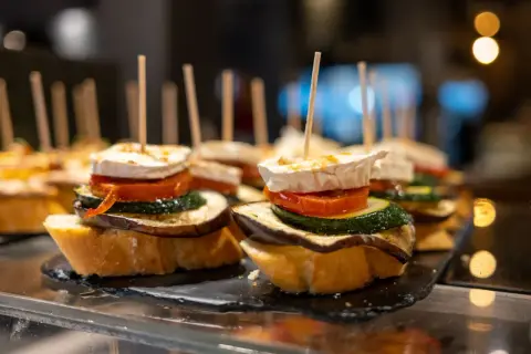 A delicious charcuterie board featuring stacked tapas on toasted bread, topped with goat cheese, tomato, zucchini, and eggplant.