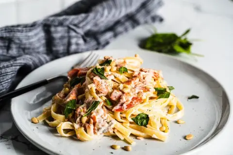 A plate of creamy smoked salmon pasta, garnished with fresh basil and pine nuts.
