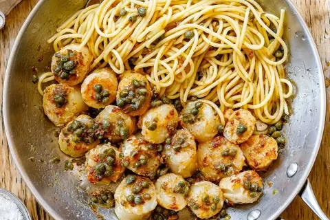 A delicious scallops and pasta recipe with white wine sauce, garnished with capers, served in a skillet.