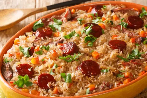 A hearty dish of rice with sauteed chorizo, tender meat, and diced carrots, garnished with fresh parsley.