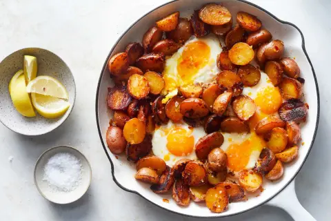 Huevos rotos: a hearty skillet dish with fried eggs nestled among crispy, golden-brown potato slices, served with lemon wedges and sea salt.