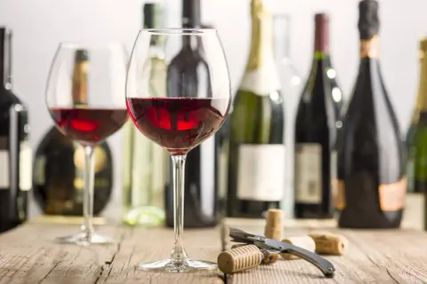 Two glasses of red wine, bottles, and corks on a wooden table. Imagine the rich, fruity mencia geschmack.